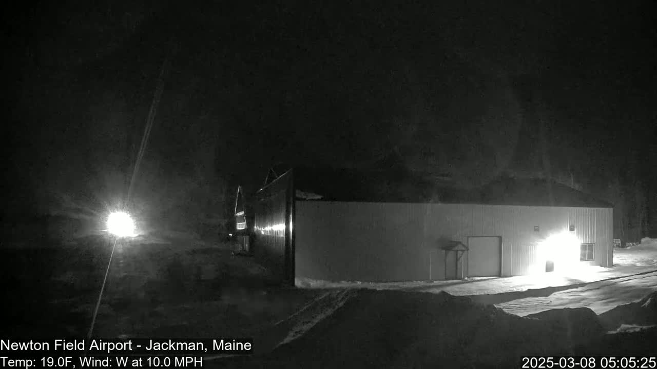 A large, light-colored building is illuminated at night in snowy conditions with a 19°F temperature and a 10 mph westerly wind.