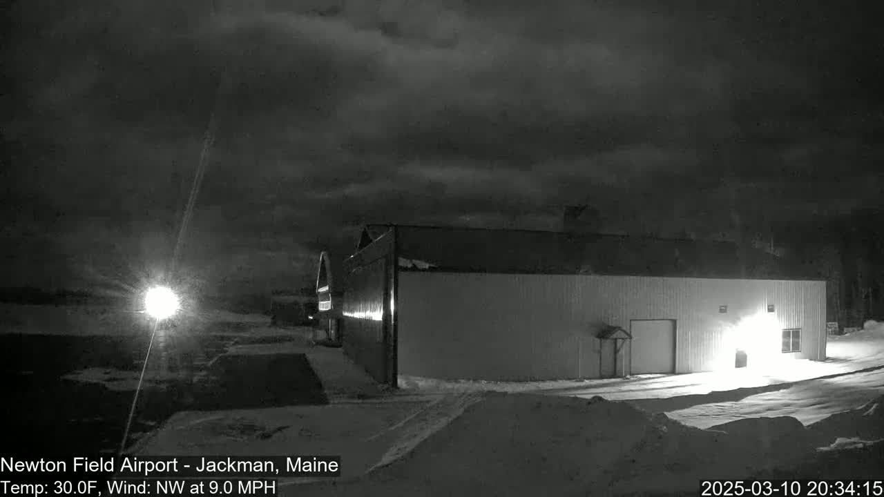 A large, light-colored building stands in a snow-covered area at night under a cloudy sky, illuminated by several lights.