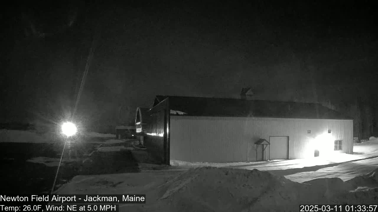 A large, light-colored building sits in a snow-covered area at night under a dark, possibly snowy sky.