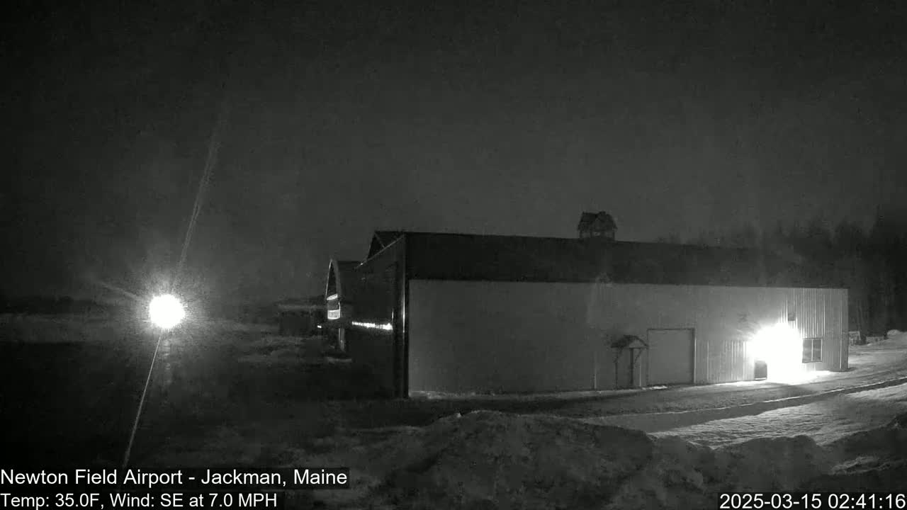 A large, light-colored building is illuminated at night in snowy conditions under a dark sky.