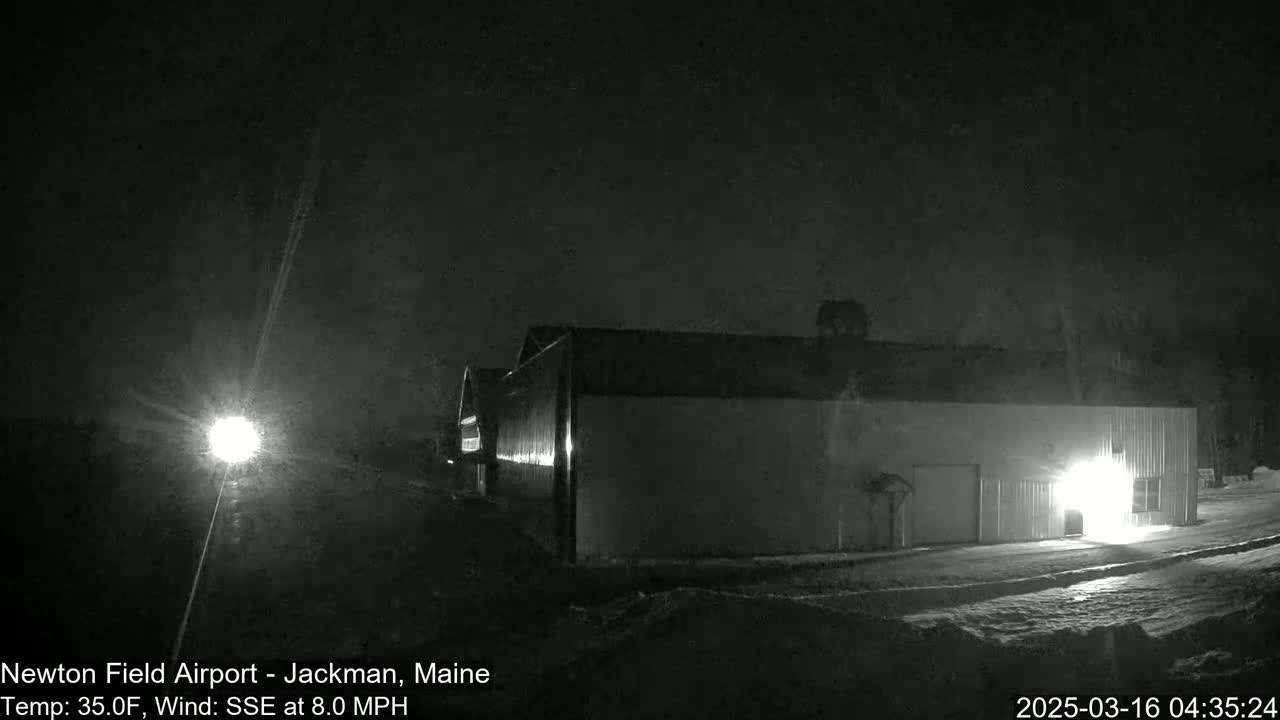 A large, light-colored building is illuminated at night in snowy conditions under a dark sky.