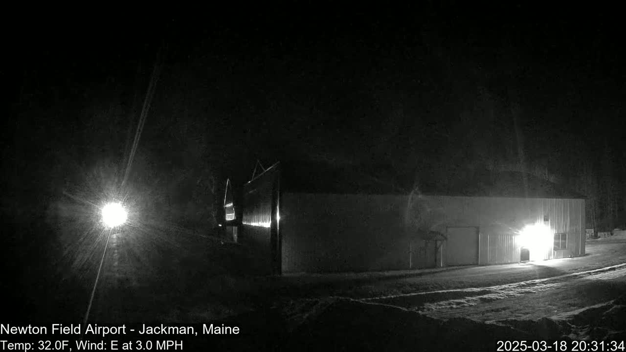 A long, low building is illuminated at night in snowy conditions with a gentle easterly wind.