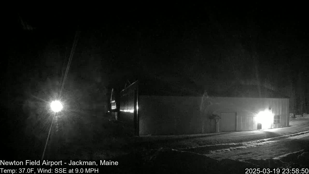 A long, dark building is illuminated by interior lights at night, under a dark sky with a 9 mph wind from the SSE, and a temperature of 37°F.
