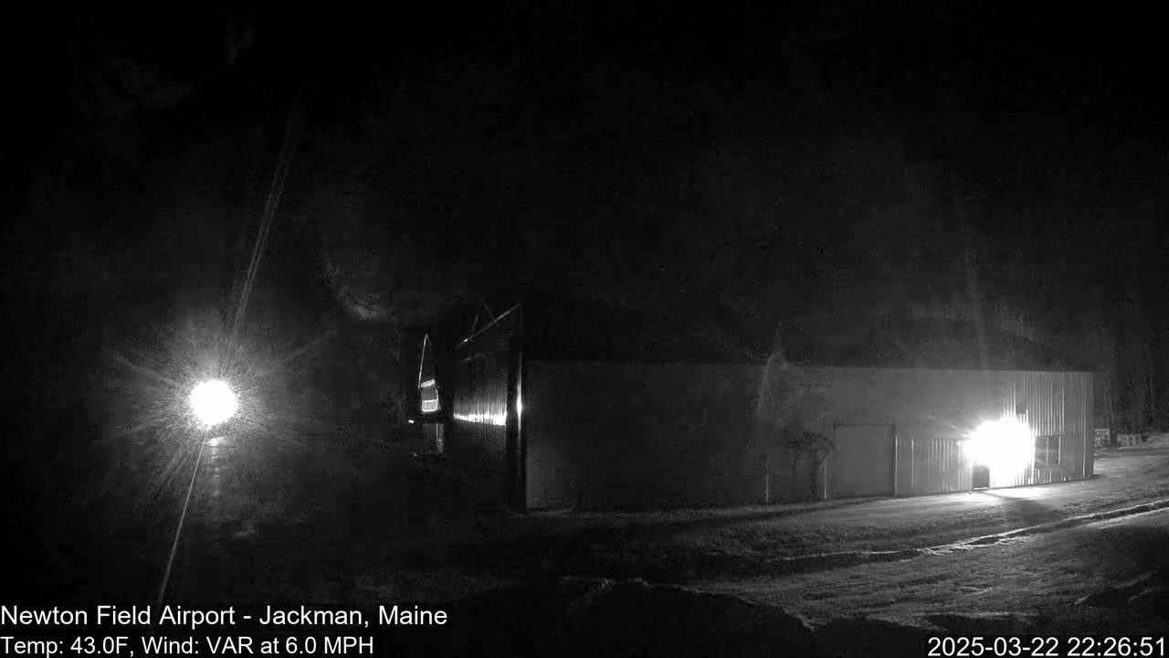 A long, low building is illuminated at night in snowy conditions with a 6.0 mph variable wind.