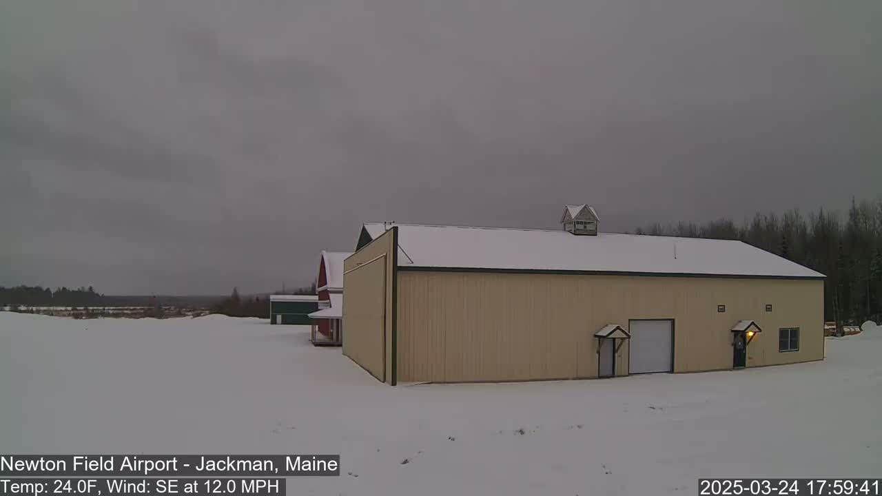 A tan building with a snow-covered roof sits in a snowy landscape under an overcast sky.