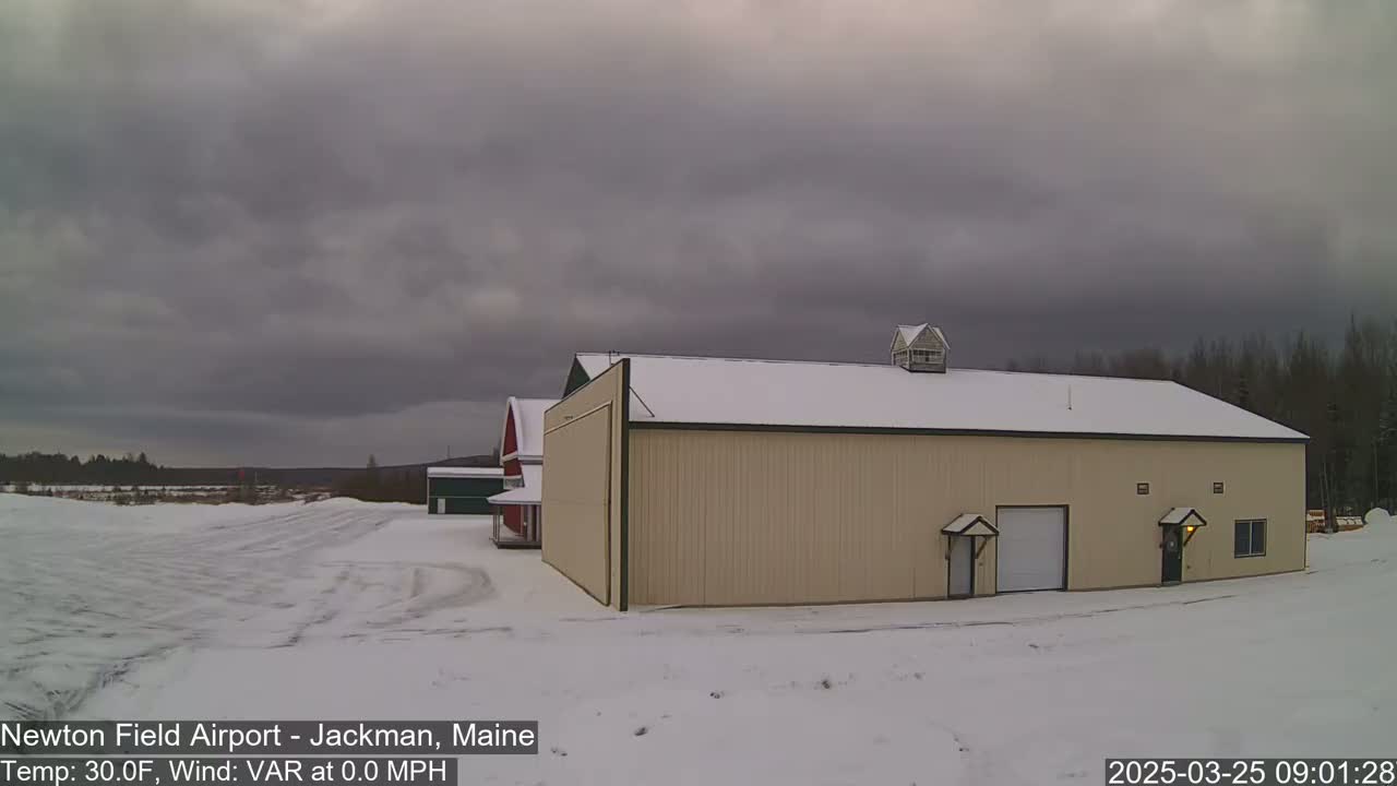 A large tan building with a snow-covered roof stands in a snowy landscape under an overcast sky.