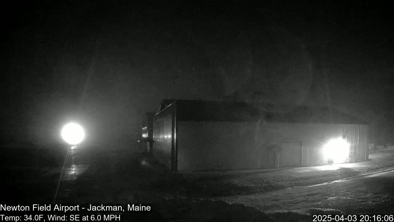 A large, dark building is illuminated by a bright light at night in foggy conditions.