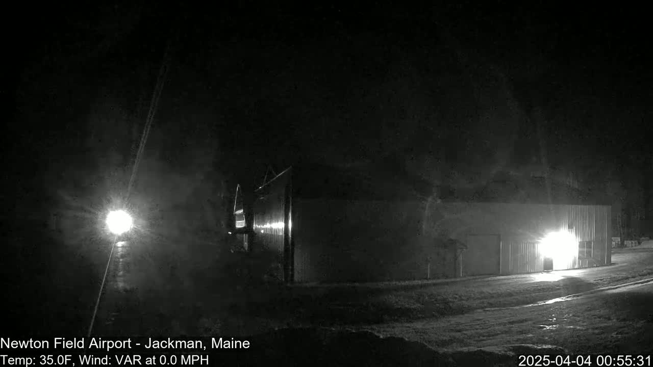 A long, dark building is illuminated by a bright light at night in snowy conditions.