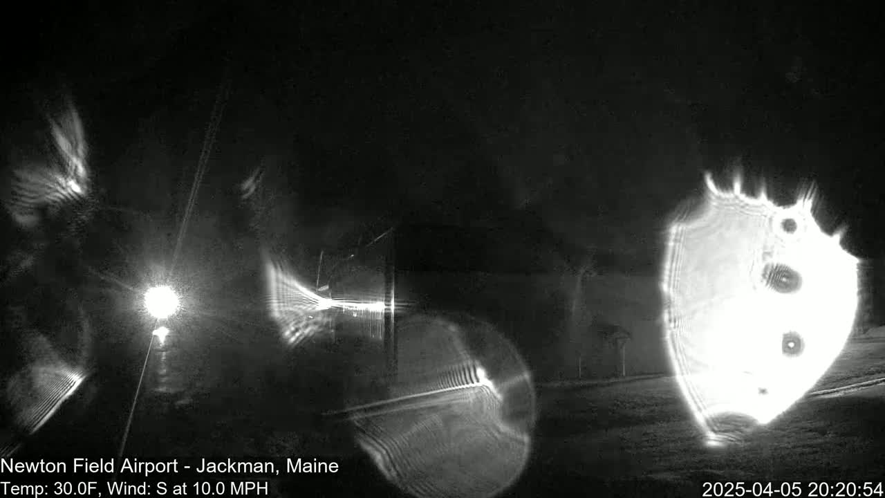 A nighttime, low-light image shows bright, distorted light sources and streaks, likely caused by camera lens flare in snowy conditions with a 30°F temperature and a 10 mph south wind.