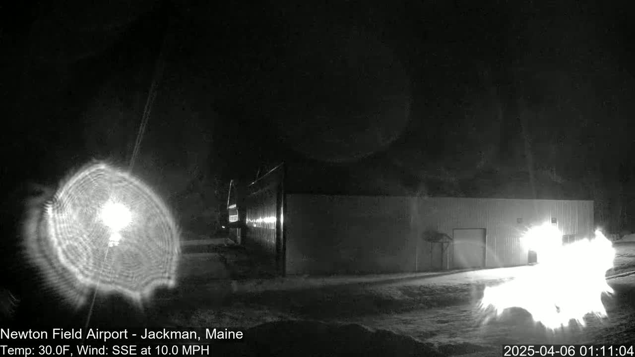 A bright light source, possibly a searchlight, illuminates a large building at night in snowy conditions with a 10 mph wind from the south-southeast.