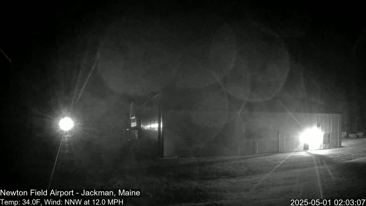 A nighttime, low-light image shows a building lit from within, under a dark sky with a northwest wind.