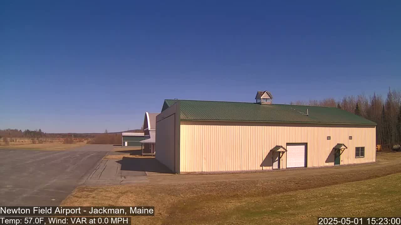 A large tan hangar with a green roof sits on an airfield under a clear blue sky.