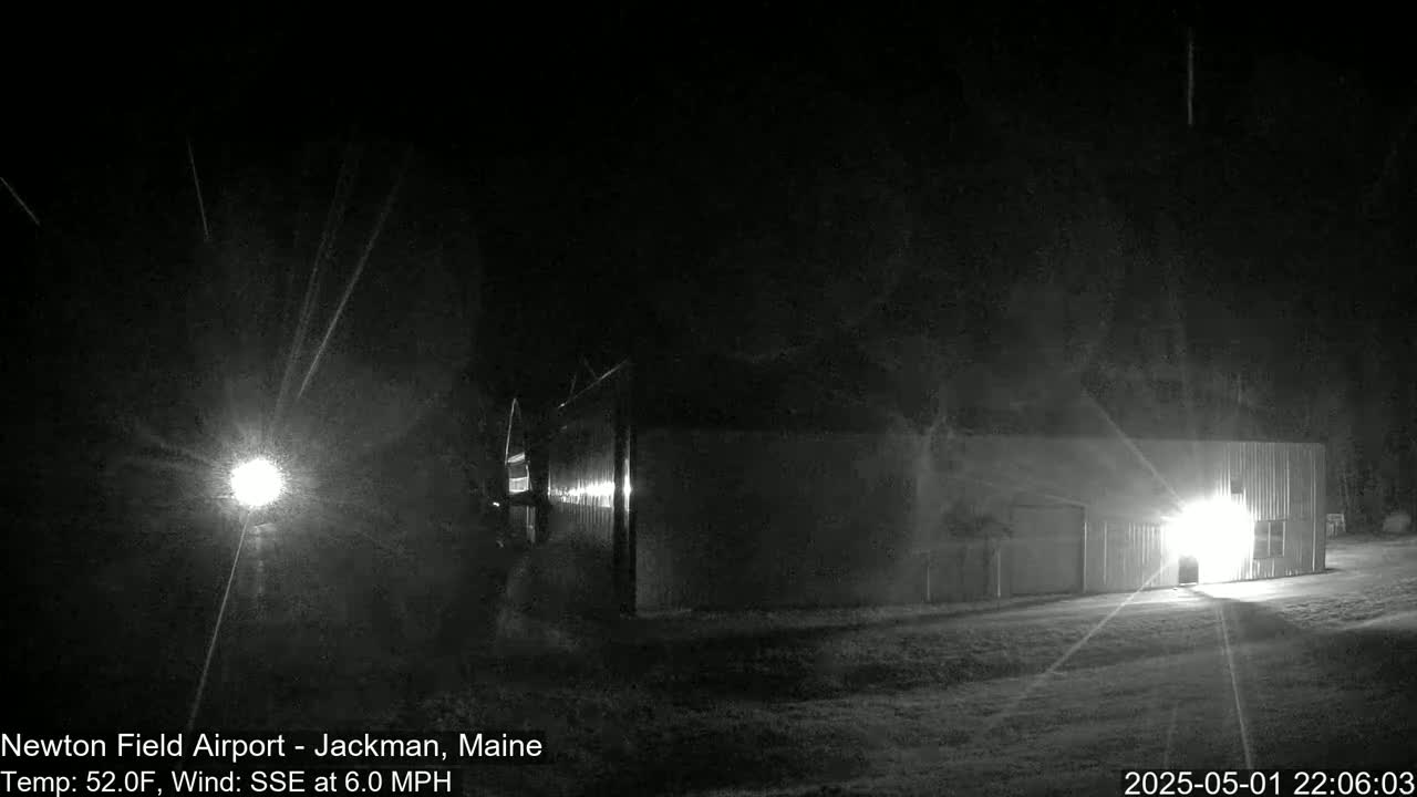 A brightly lit building is visible at night in snowy conditions, with a light source in the distance casting beams of light.