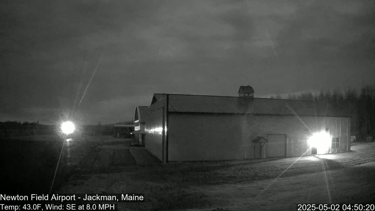 A large, dark building is illuminated by lights at night under a mostly cloudy sky.