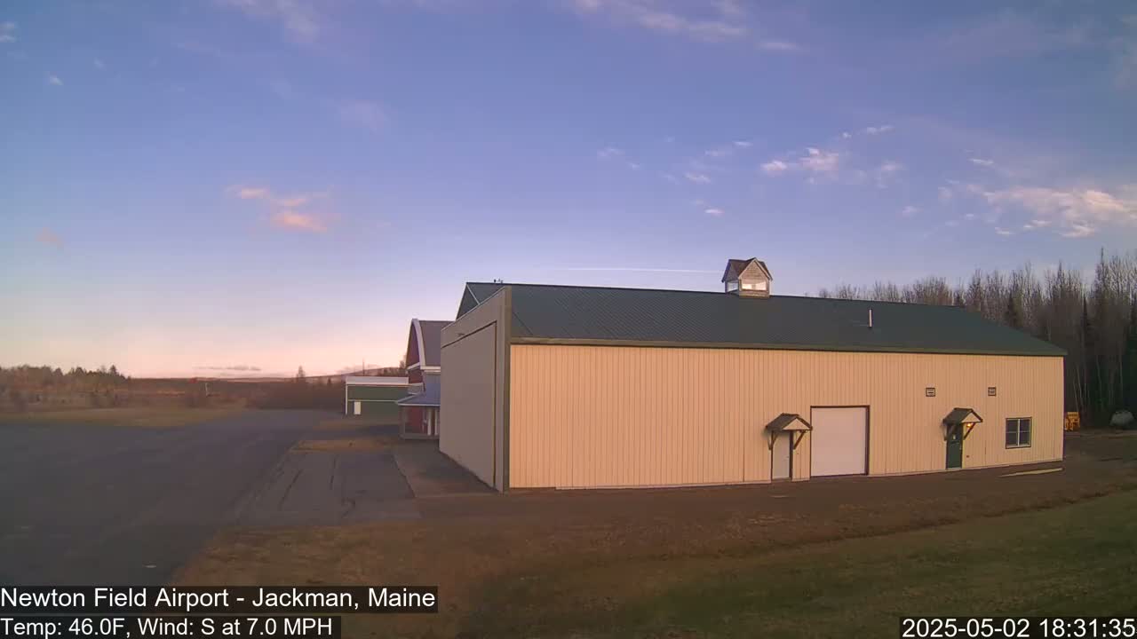 A large tan hangar with a green roof sits on an airfield under a clear, twilight sky.