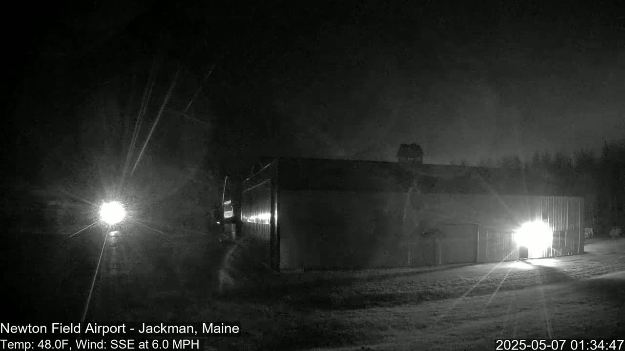 A large, dark building is illuminated by lights at night in snowy conditions.