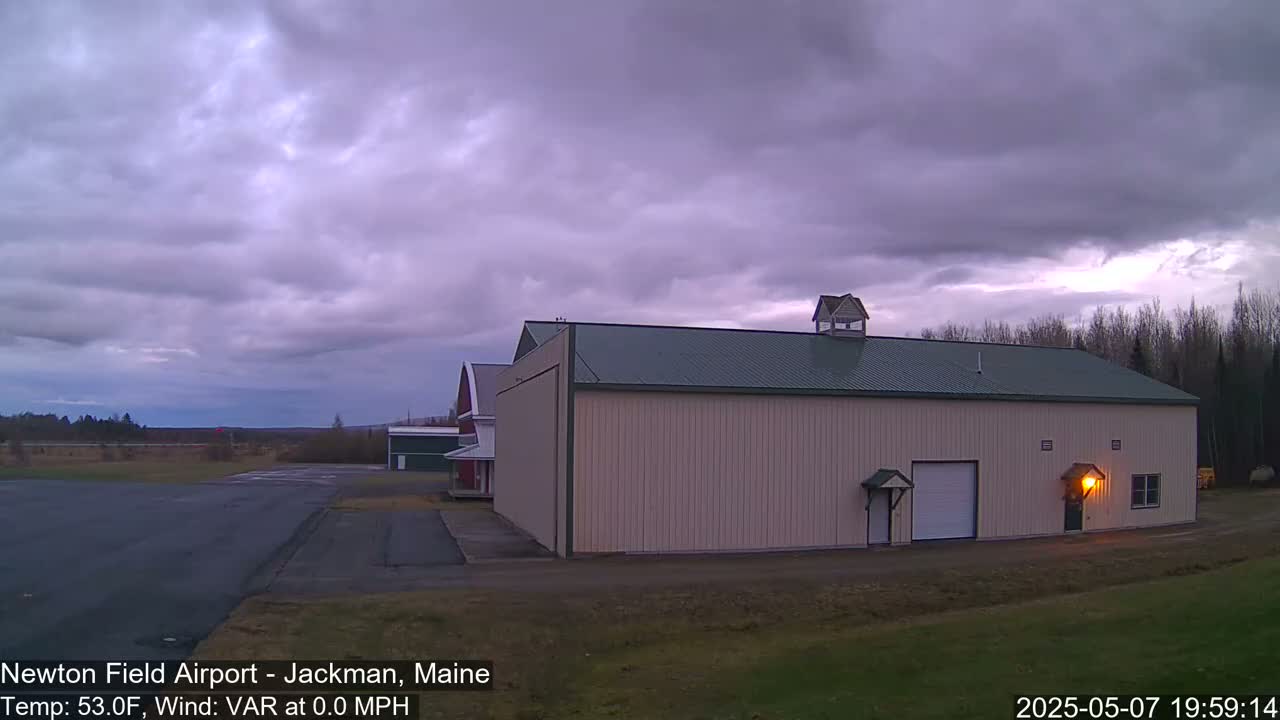 A large tan hangar sits on an airfield under a cloudy, dusky sky.