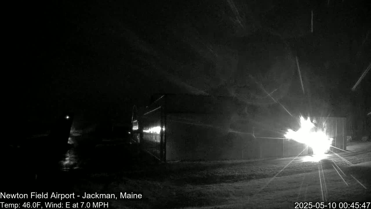 A bright fire illuminates a dark, snowy nighttime scene near a building.