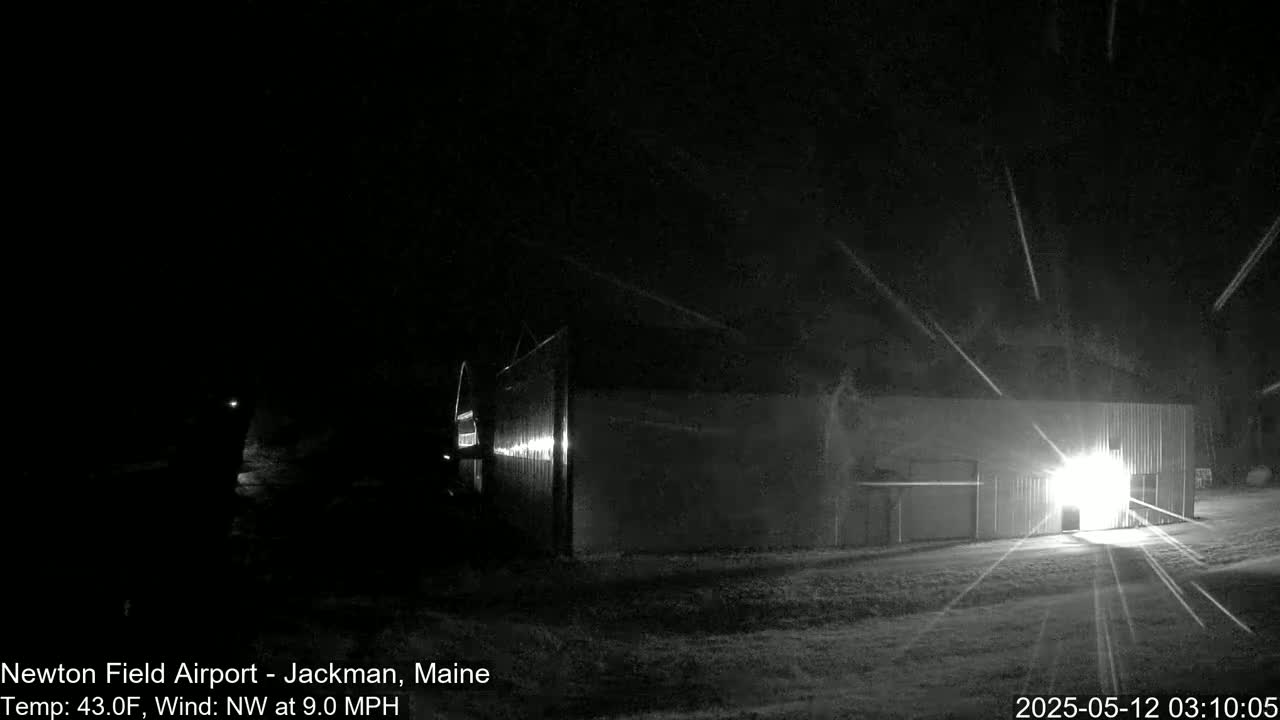 A brightly lit hangar stands in a snowy, nighttime landscape with a northwest wind.