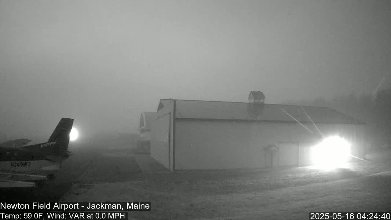 A small airplane is parked near a large hangar in dense fog.