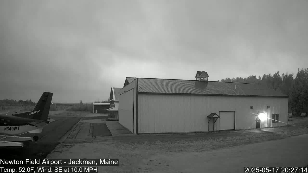 A small airplane sits on a tarmac next to a large hangar under an overcast sky.