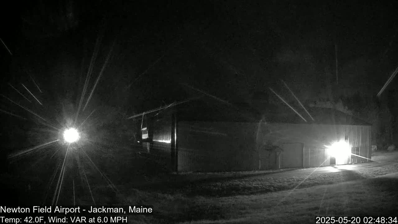 A large, dark building is illuminated at night by a bright light source, under a dark sky with light streaks.