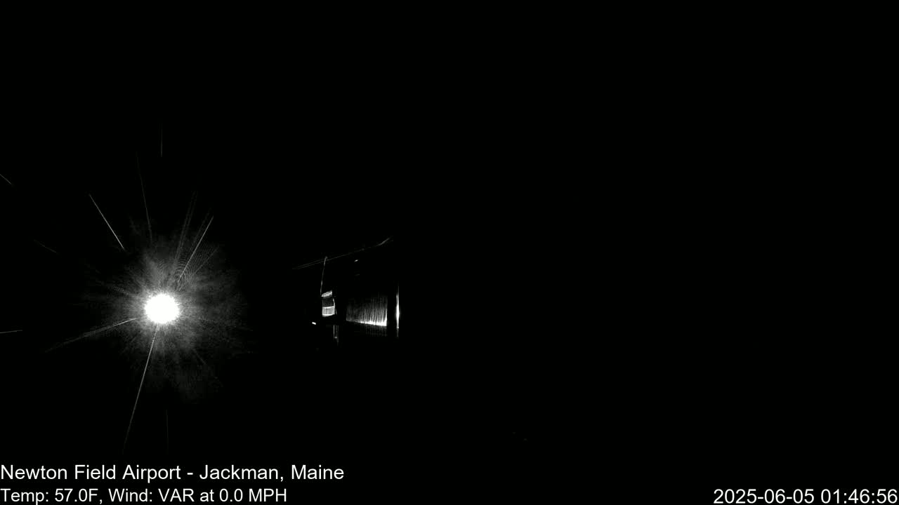 A bright light shines in the darkness, illuminating a building and creating starburst-like streaks.