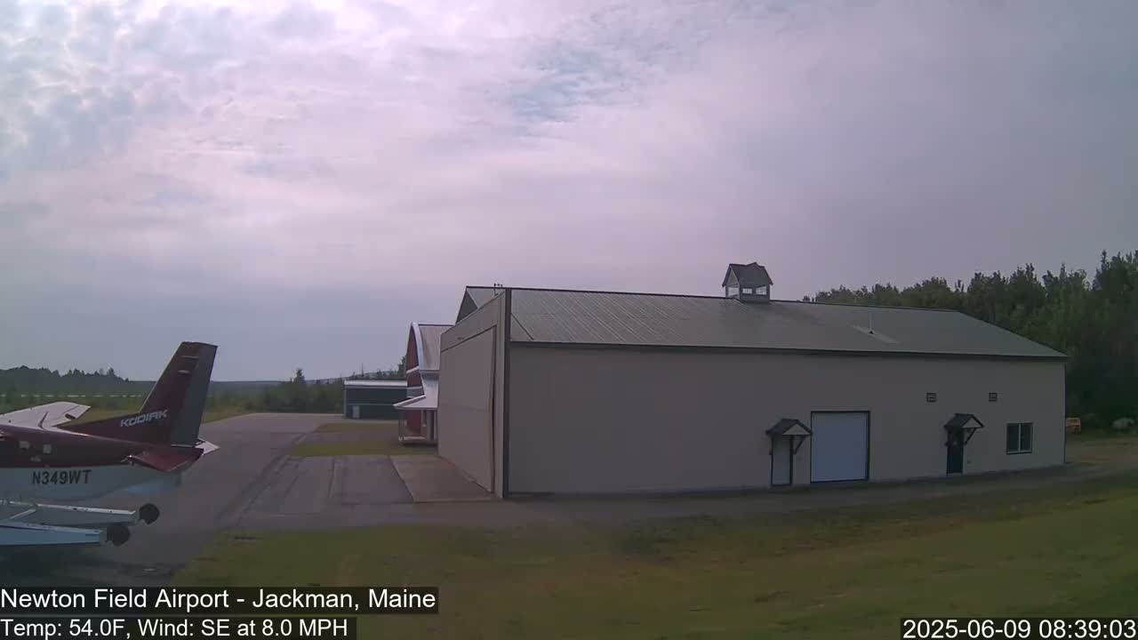 A small airplane is parked on an airfield next to a large hangar under an overcast sky.