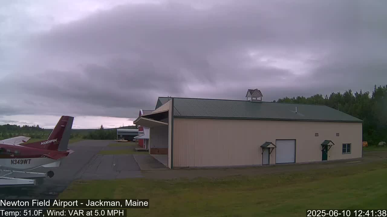 A small airplane is parked on an airfield next to a large tan building under an overcast sky.
