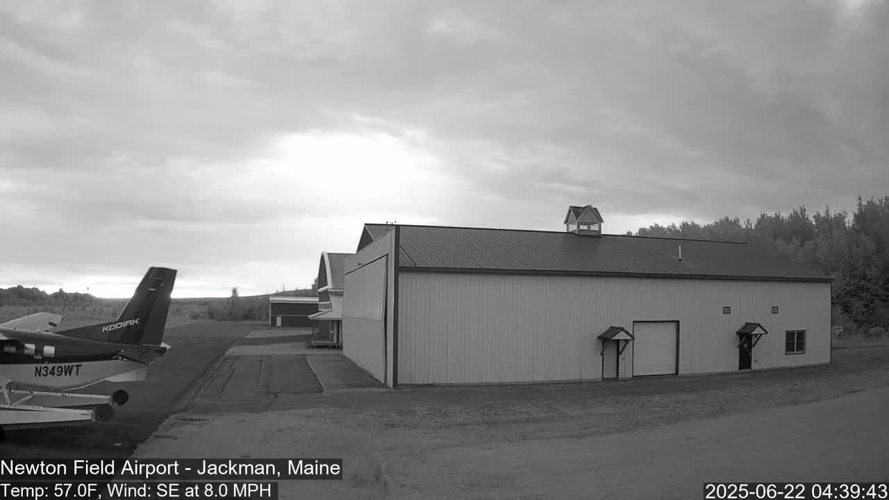 A small airplane is parked on an airfield next to a large hangar under an overcast sky.