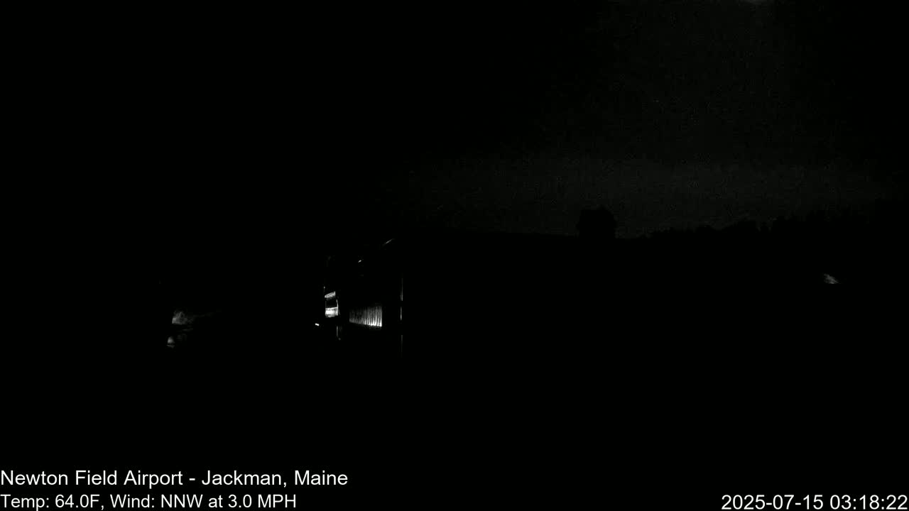 A dimly lit, dark nighttime scene shows a building in the distance under a mostly clear sky with a slight north-northwest wind.