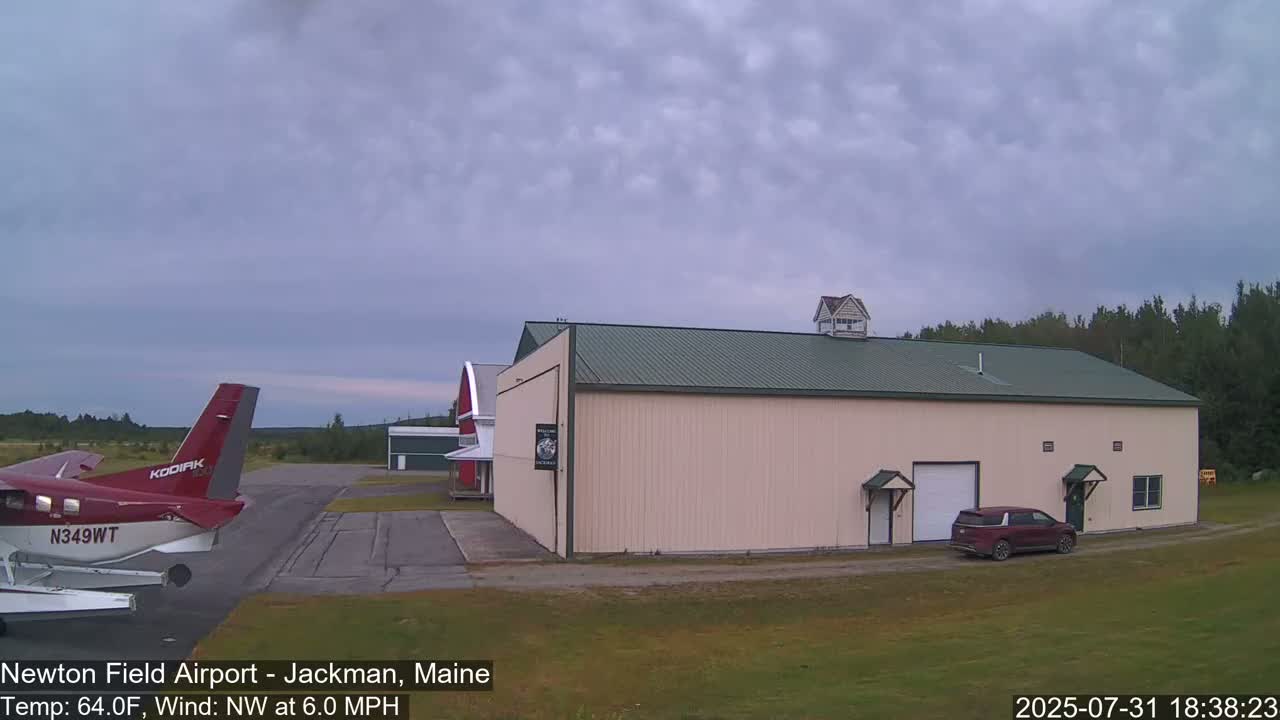 A red airplane is parked on an airport tarmac next to a large beige building under a cloudy sky.