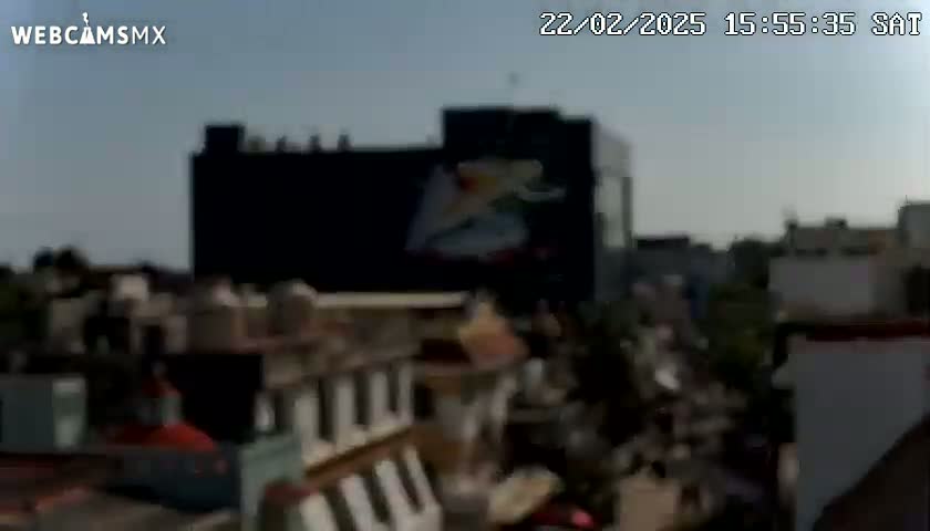 A large building with a dark billboard featuring a light-colored graphic is visible, surrounded by other buildings under a mostly clear sky.