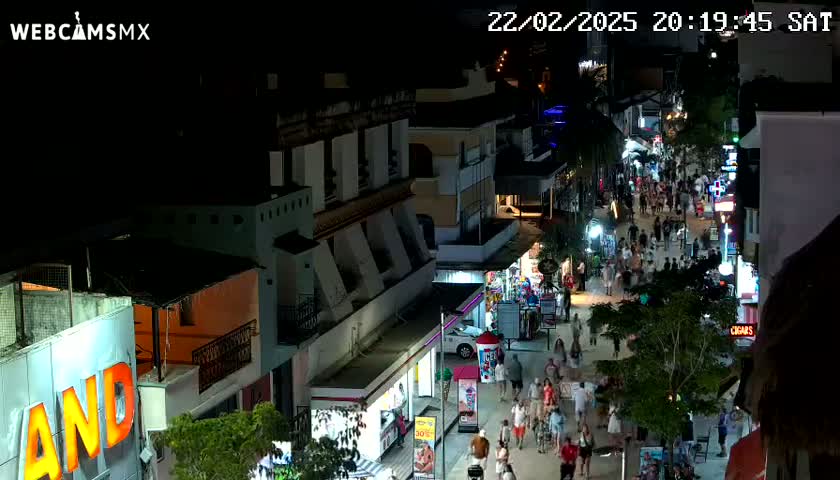 A nighttime aerial view of a bustling pedestrian street lined with shops and buildings, under clear skies.