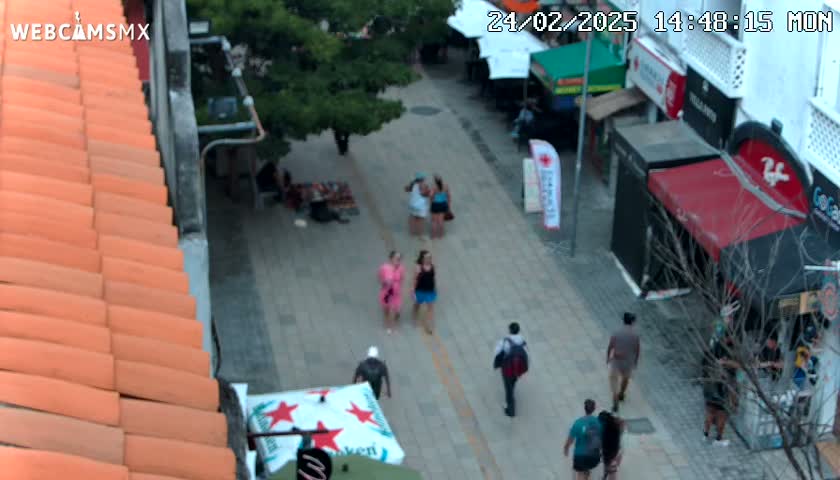 An outdoor pedestrian street scene on a partly sunny day shows several people walking among shops and restaurants.