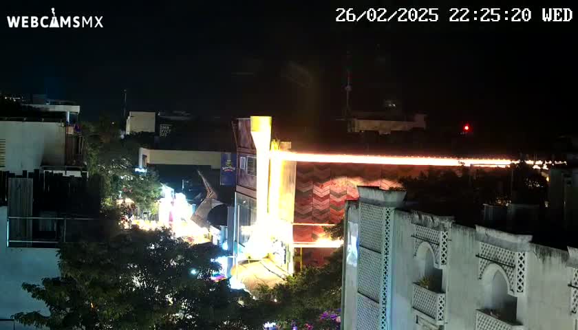 A nighttime, overhead view of a brightly lit street scene with buildings and trees, under a clear, dark sky.