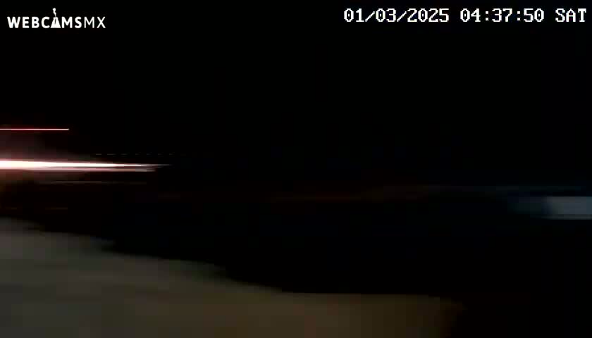 A nighttime image shows light trails of vehicles passing by on a dark road.