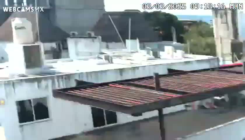 A mostly sunny day reveals a rooftop view of several buildings with a metal awning structure in the foreground.