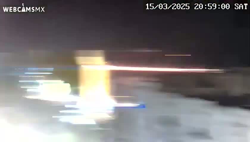 A blurry nighttime image shows bright streaks of light, possibly from headlights, moving across a dark, snowy or hazy scene.
