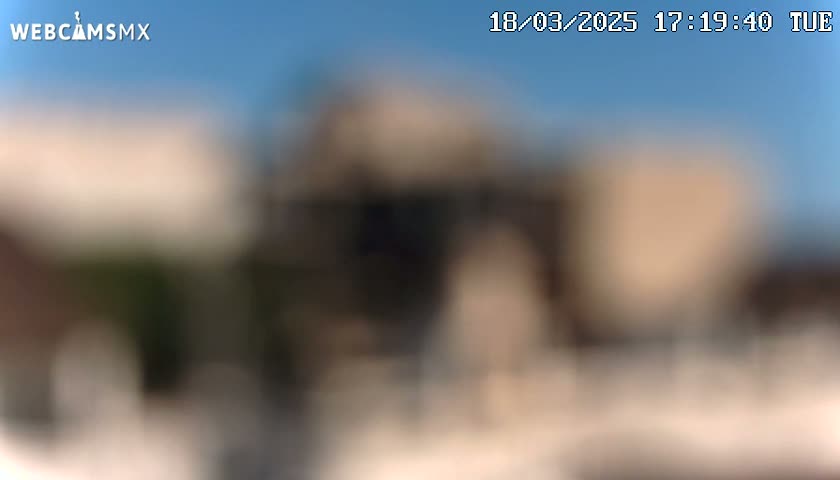 An out-of-focus image shows a blurry view of buildings under a clear blue sky.