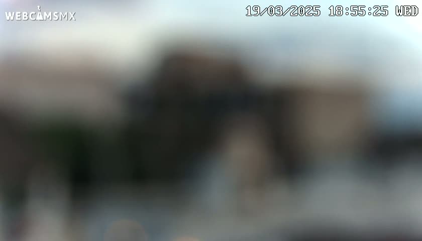 A blurry image shows an indistinct outdoor scene under a mostly cloudy sky.