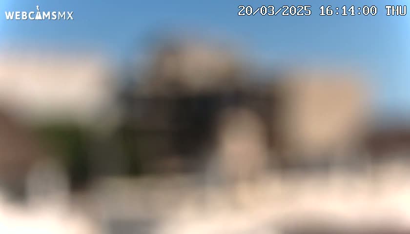 A blurry outdoor image shows indistinct structures under a clear blue sky.