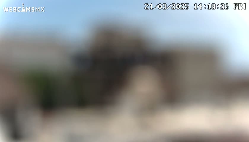 A blurry outdoor image shows a light-colored building under a clear sky.