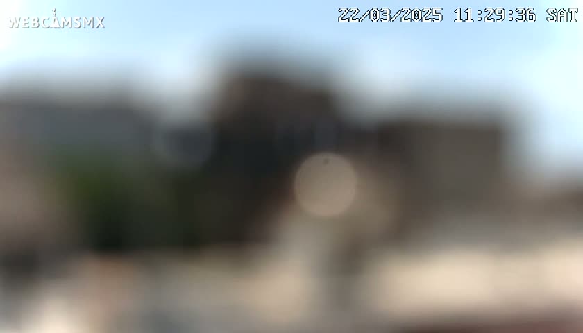 A blurry image shows an out-of-focus view of buildings under a mostly clear sky.