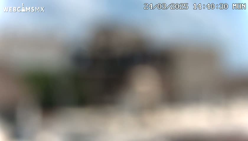A blurry outdoor image shows an indistinct building under a mostly clear sky.