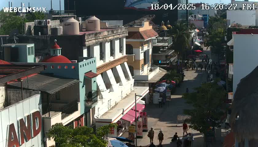 A sunny day reveals a street scene of multi-story buildings, shops, and pedestrians, viewed from an elevated perspective.