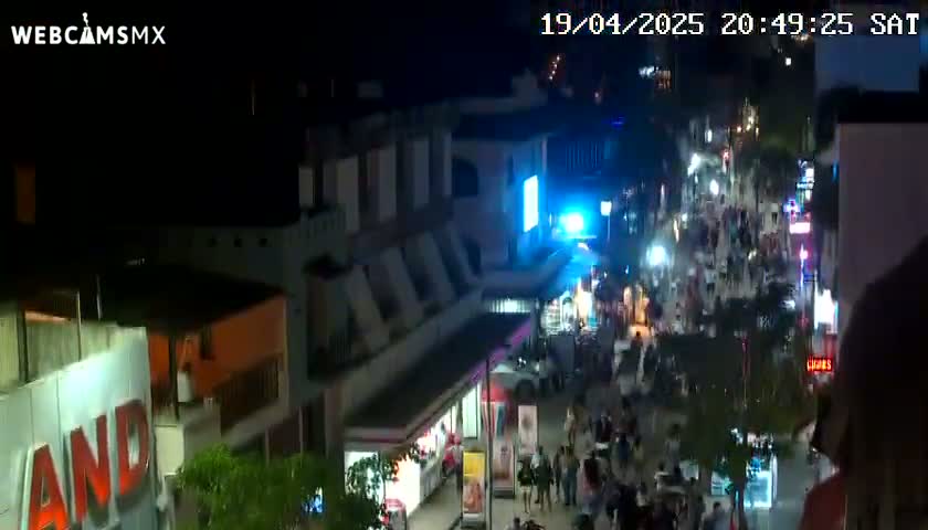 A nighttime, high-angle view shows a crowded pedestrian street with brightly lit buildings and shops.