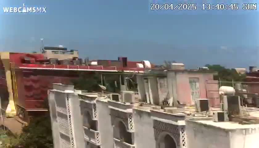 A mostly sunny day reveals a view of a city with several buildings, including a large red structure and several light-colored buildings with intricate designs.
