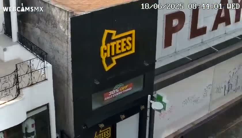 A high-angle view shows a black building with a yellow arrow and the word "CITEES" on it, next to a building with graffiti and a partially visible sign that says "PLAY".