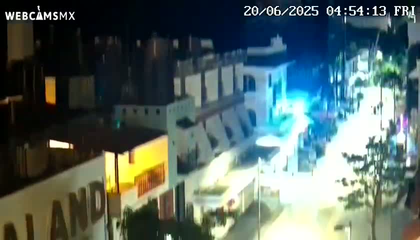 A nighttime, high-angle view shows a street scene with brightly lit buildings and some people moving around.